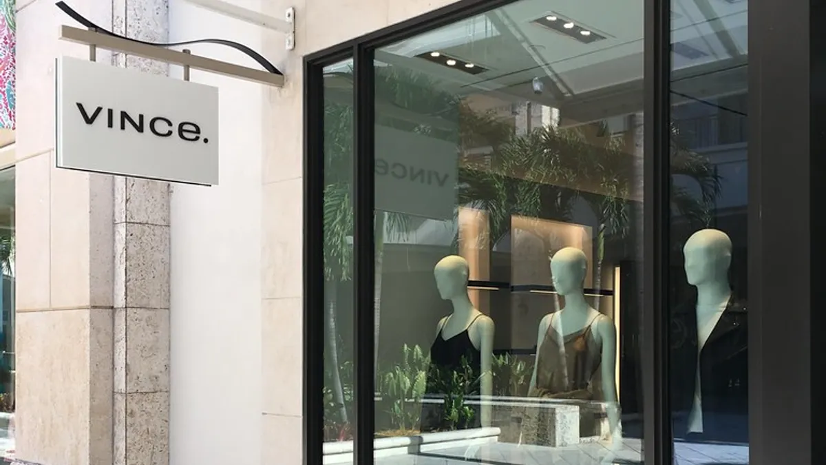 A view of a Vince store from outside. The sign is visible as well as three mannequins through the window.