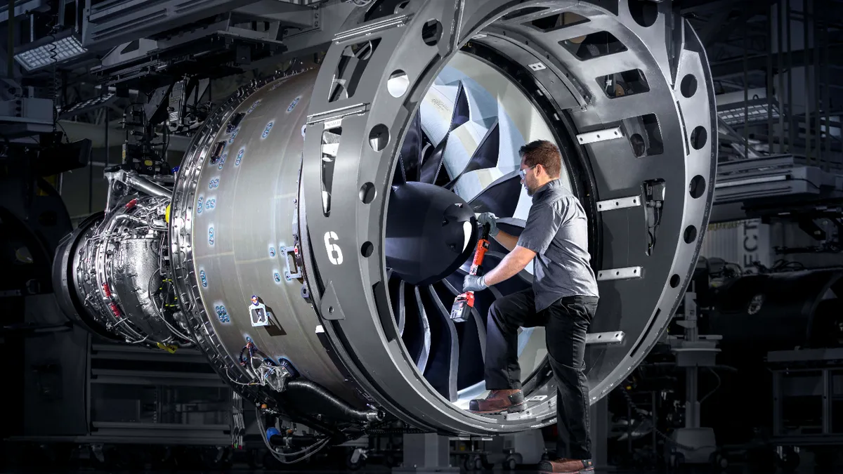 A person wearing goggles and gloves in a dark gray uniform working on a jet engine.