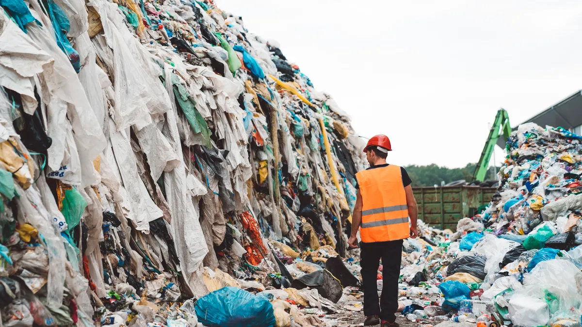 A worker walks through two massive piles of trashed clothing