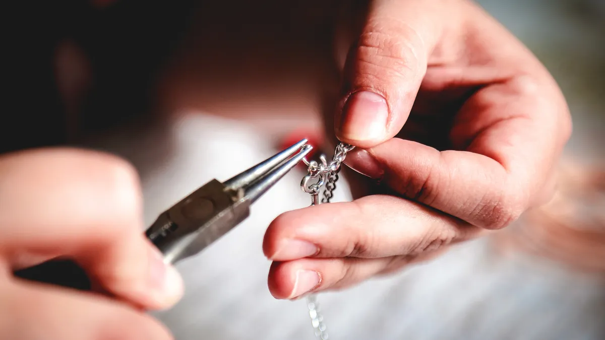 The hands of a young woman are shown crafting a silver jewelry chain.