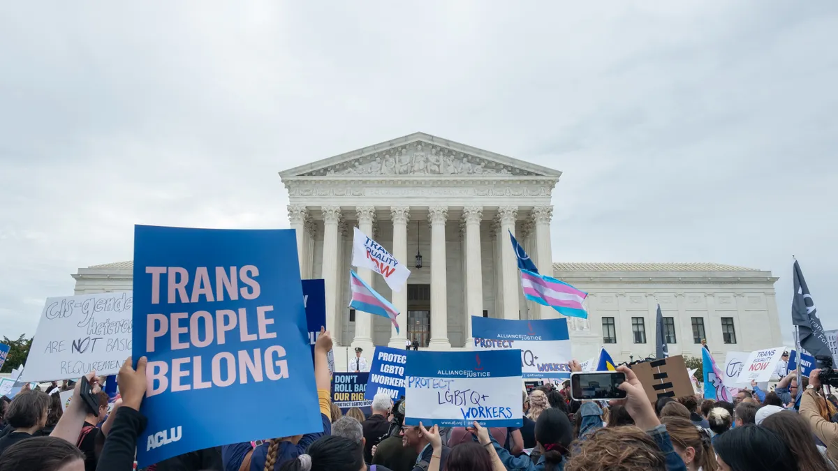 Individuals stand outside the U.S. Supreme Court. A sign reads "Trans People Belong."