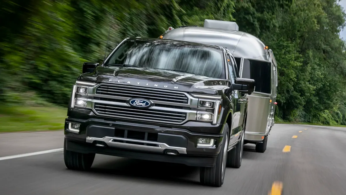 A 2024 F-150 Platinum driving on a road towing a trailer.