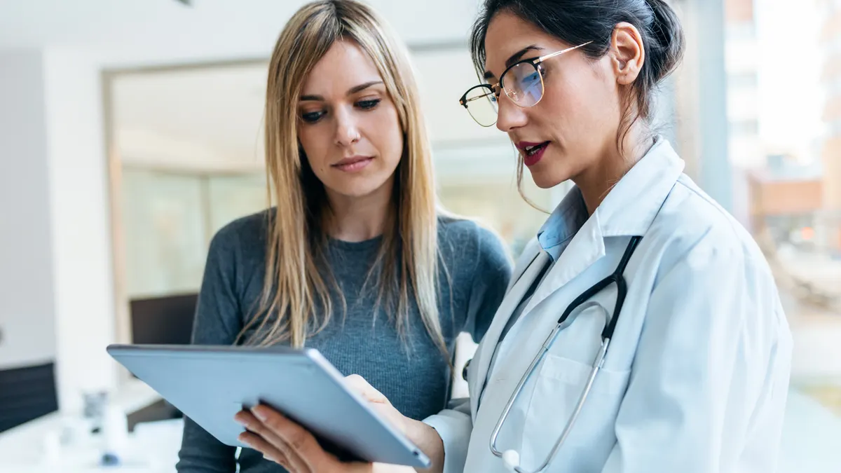 A doctor in a white coat shows a patient information on a tablet.