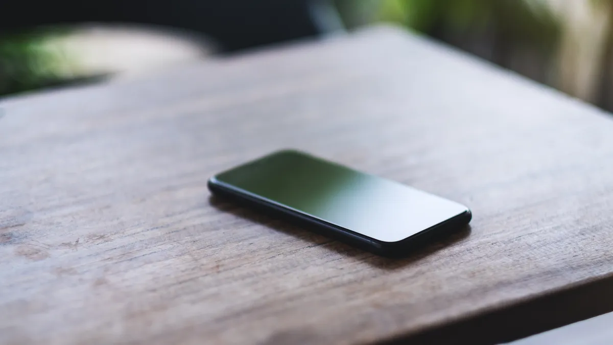 A mobile phone sits on a wooden table.