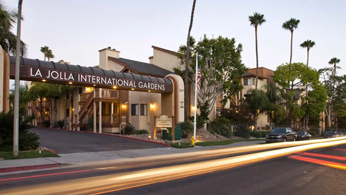 Entry to tan apartment community with tree-lined street in the foreground.