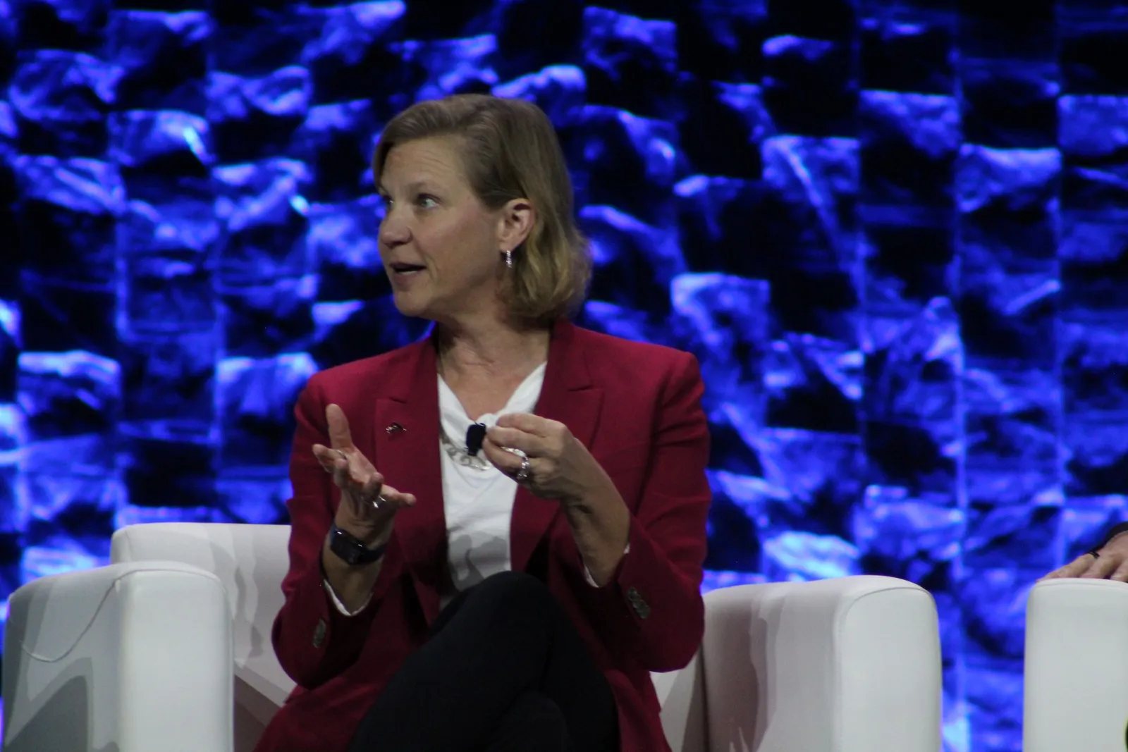 A person sits in a white chair and speaks while holding a hand open.
