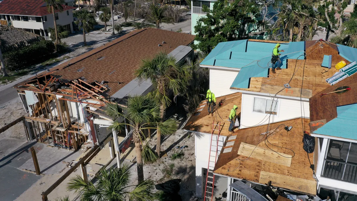 Three construction workers stand on the roof of a house being rebuilt.