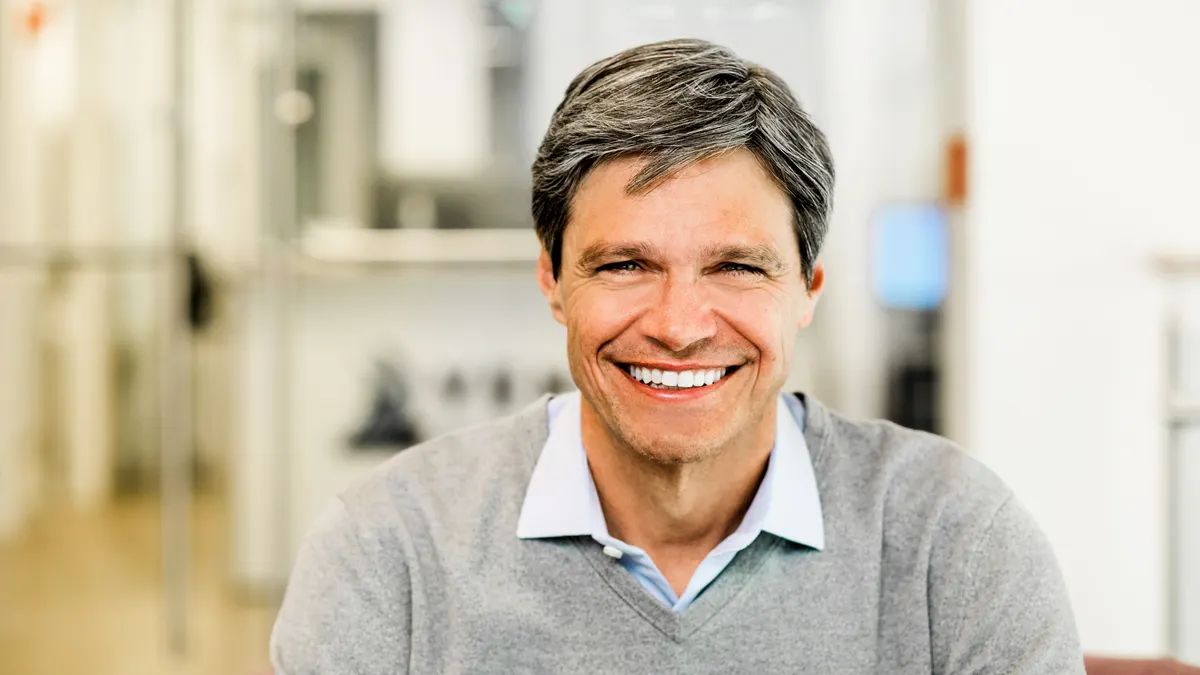 A brown and gray-haired man smiles at the camera.