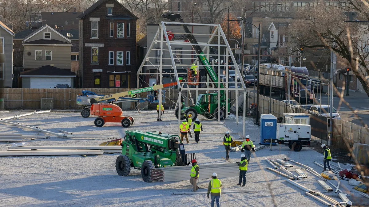 Workers construct a steel framed tent using construction equipment