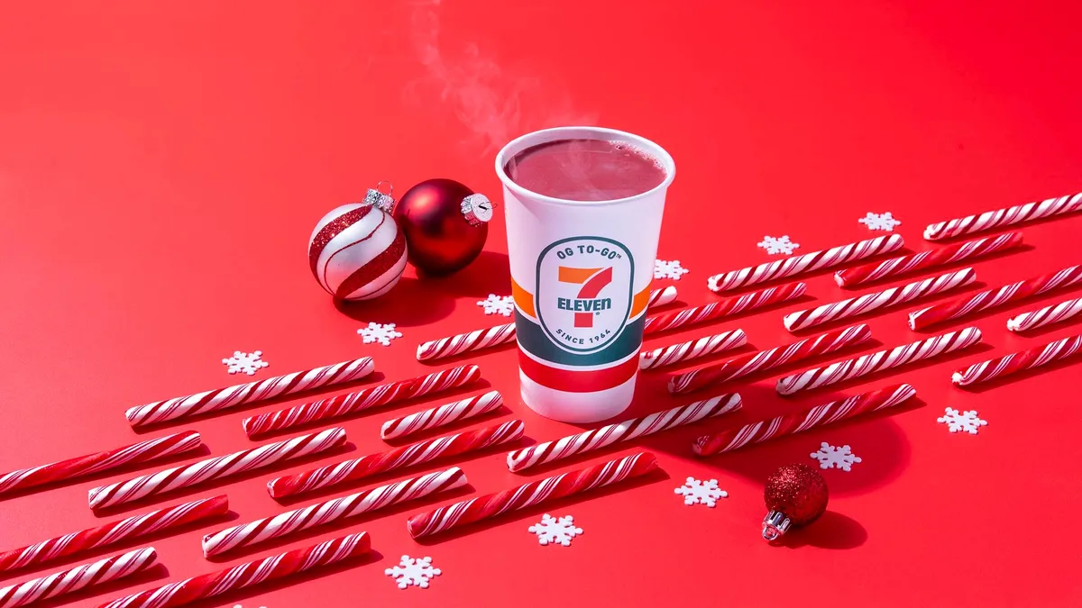 A photo of a cup of 7-Eleven cocoa on a red background with a few candy canes and Christmas tree ornaments on it.