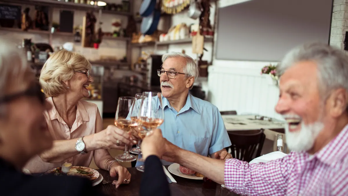 An image of people with gray hair holding up wine glasses while at a restaurant