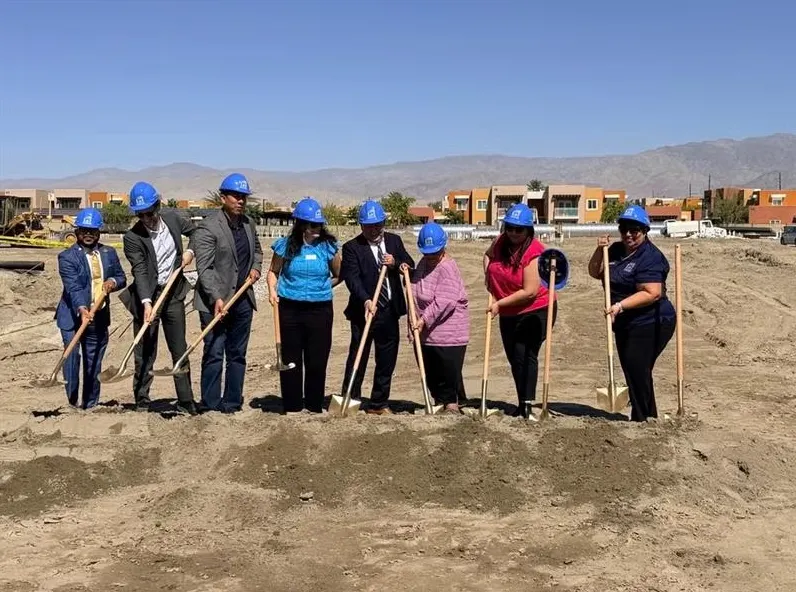 People with hard hats stand with shovels in a pile of dirt.