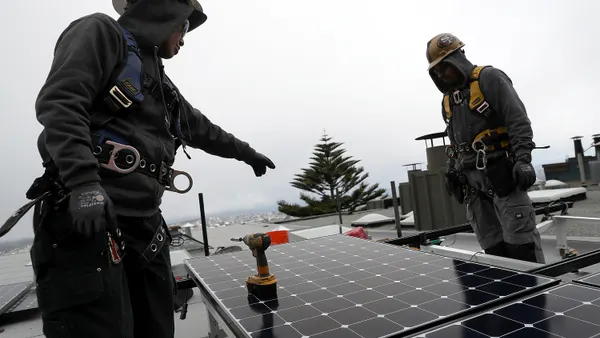 A worker points to a solar panel while another worker looks on.