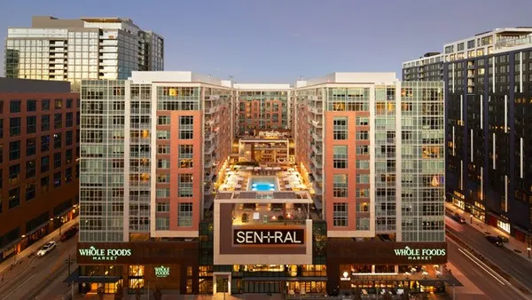 Picture of modern high-rise apartment towers with pool in between and Whole Foods on the first floor.