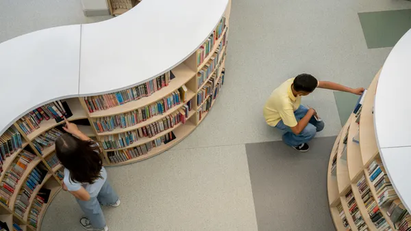 An above camera angle of a school library showing two students near book shelves.