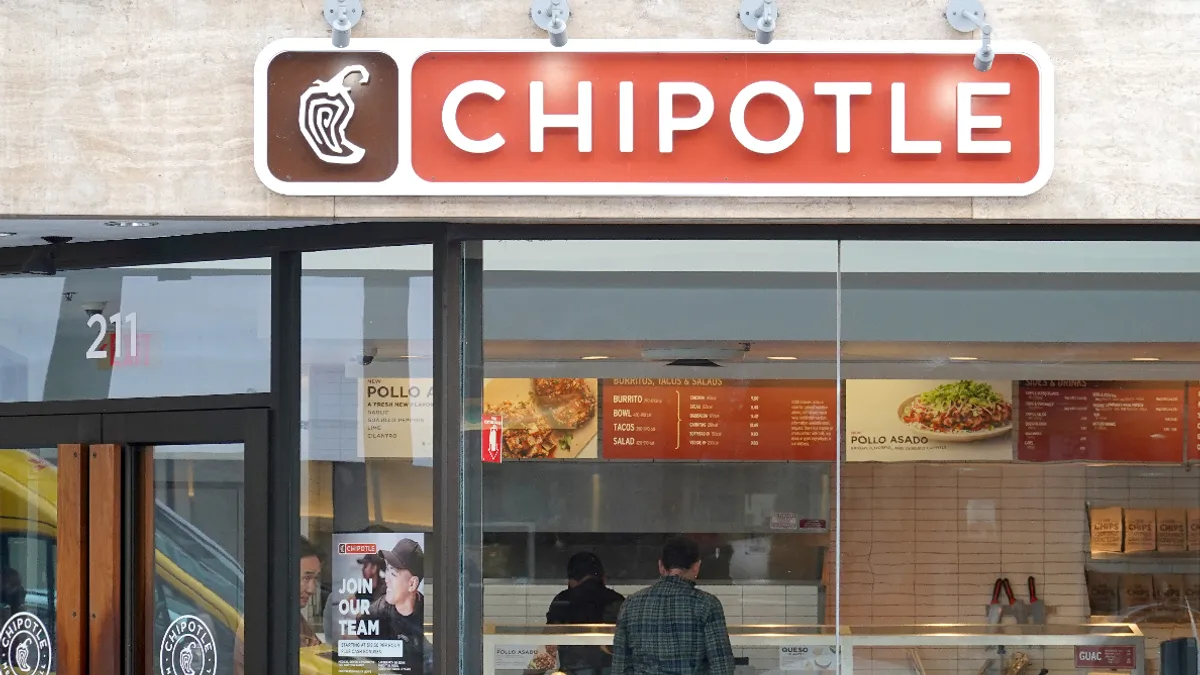 A bank of windows below a red sign that says "Chipotle." A man stands in the background inside the restaurant.