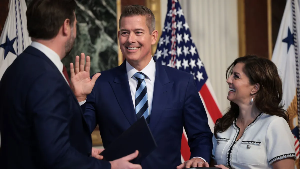 Three people stand by U.S. flags as one raises his hand, the other on a bible.