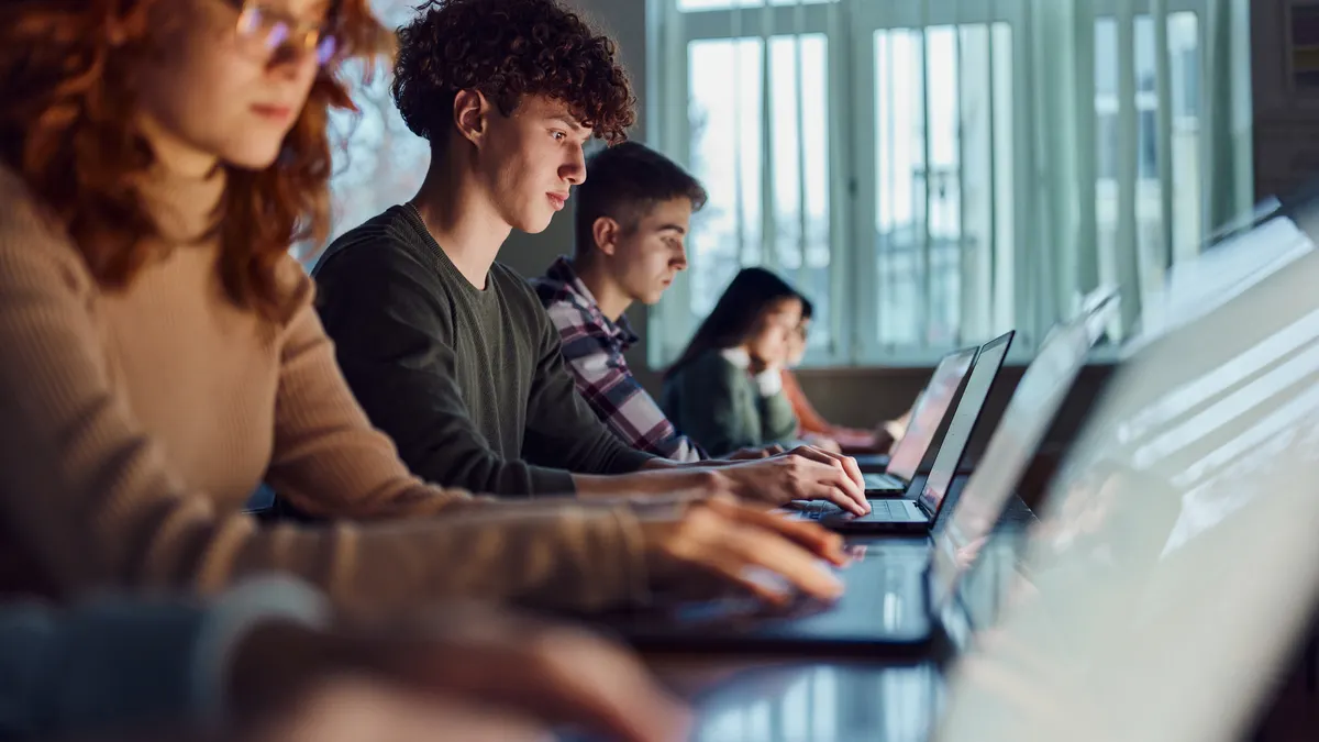 A group of high school students studies over laptops in a class at school.