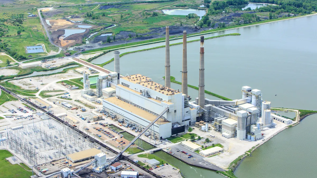 An aerial view of a coal-fired power plant with three smokestacks next to a lake.