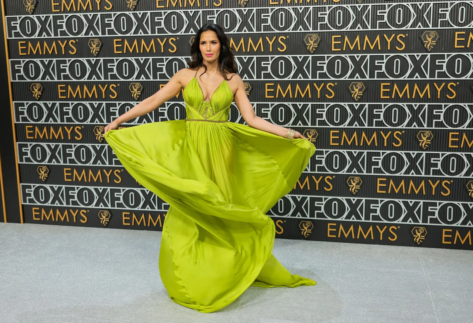 A person twirls in a bright green gown on a silver carpet.