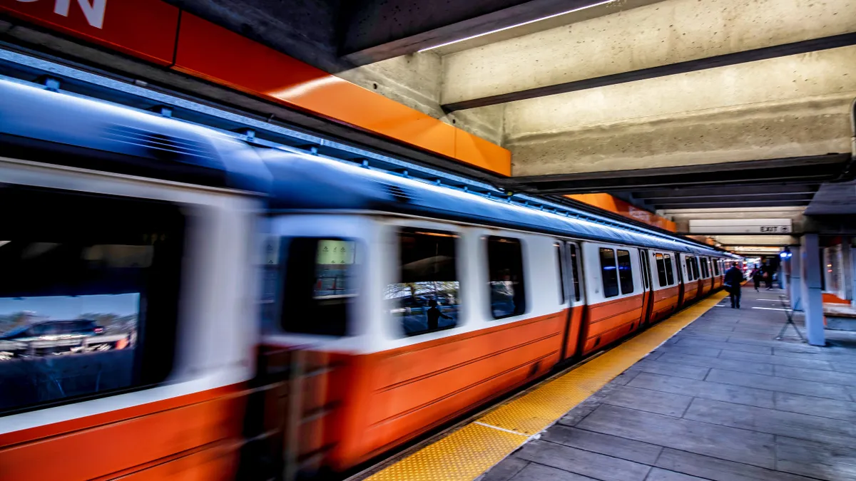 An orange and white subway train in an underground station in Boston.