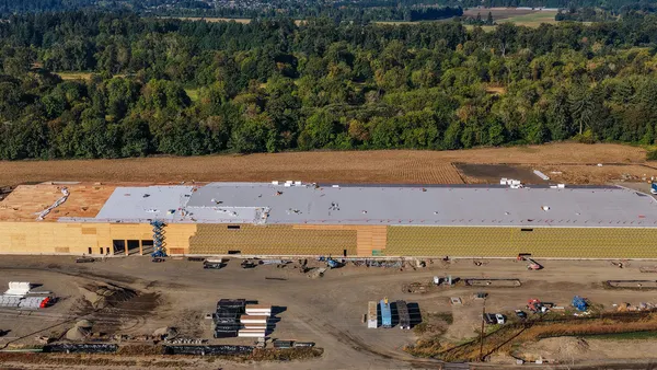 A far-out skyshot of a large facility that sits on a new construction site. The long building stretches to the edge of the frame.