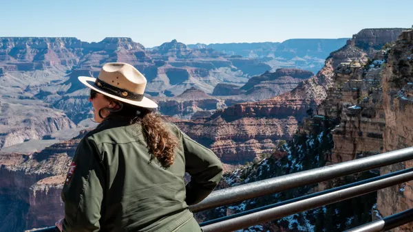 A woman park ranger's back is to the camera as she looks out from the Grand Canyon's South Rim.