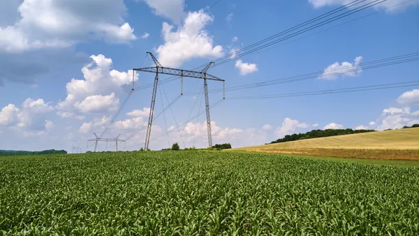 High-voltage tower with electric power lines between green agricultural fields.