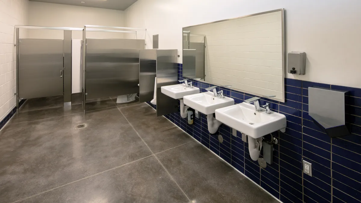 A school bathroom showing three sinks, a urinal and stalls.