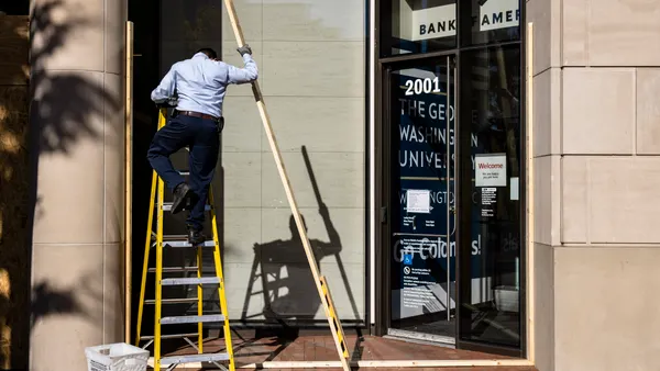 A maintenance worker climbs a ladder outside a building.