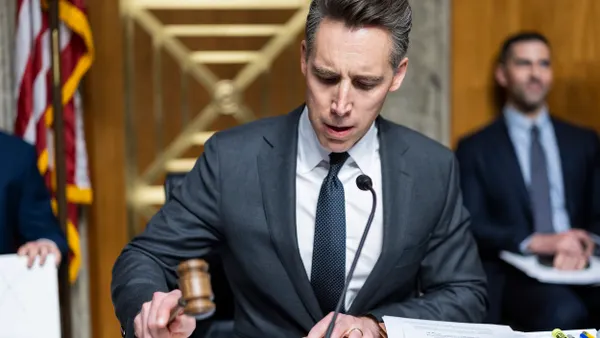 A person wearing a suit bangs a gavel with a U.S. flag behind them.