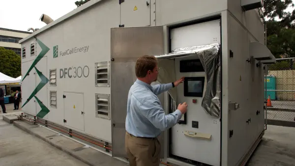 A person works on a panel of a large metal box that says Fuel Cell Energy DFC 300.