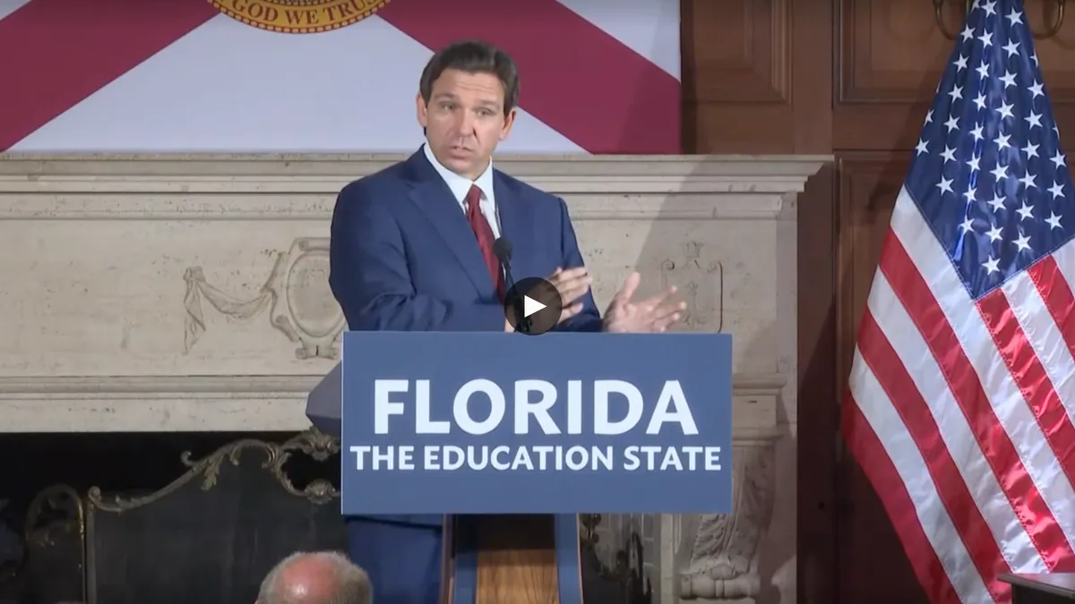 A man in a suit speaks at a podium in front of the Florida state flag.