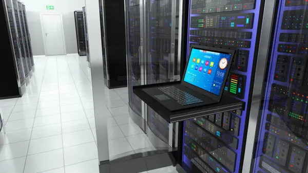 A laptop computer with a lit screen rests on a shelf in a computer server room.
