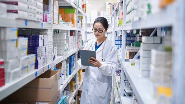 A pharmacist takes inventory of prescription drug cartons using a digital tablet.