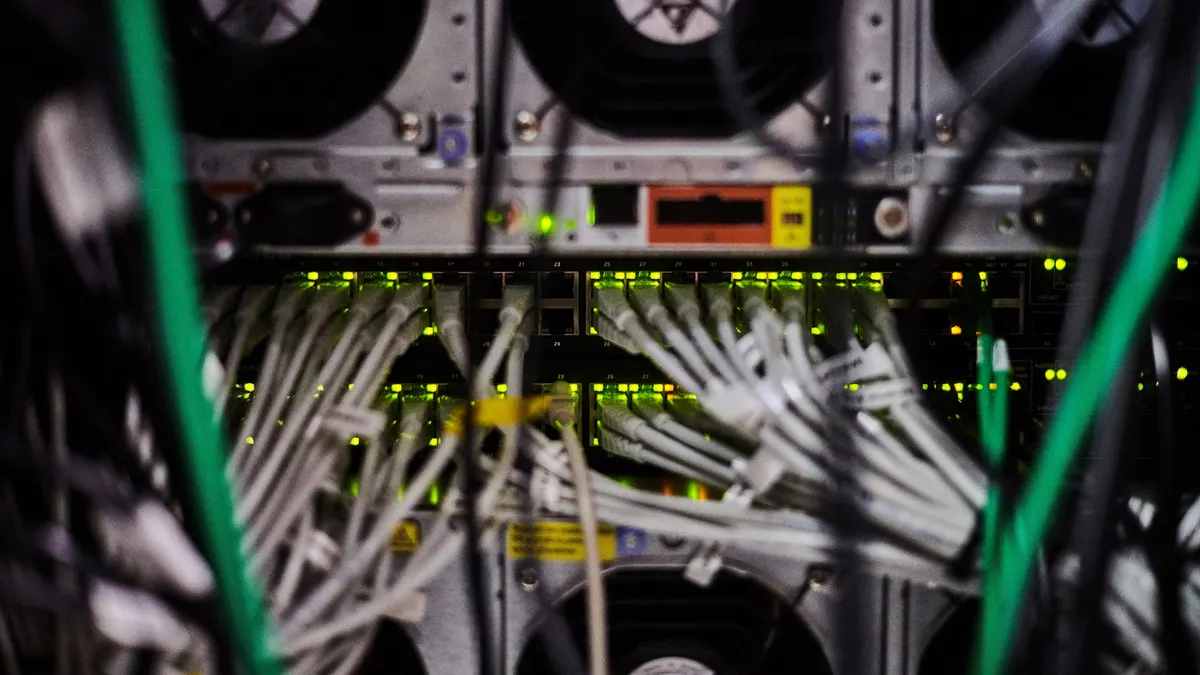 Various Ethernet cables are plugged in a row on the back of a server, with wires in the foreground.