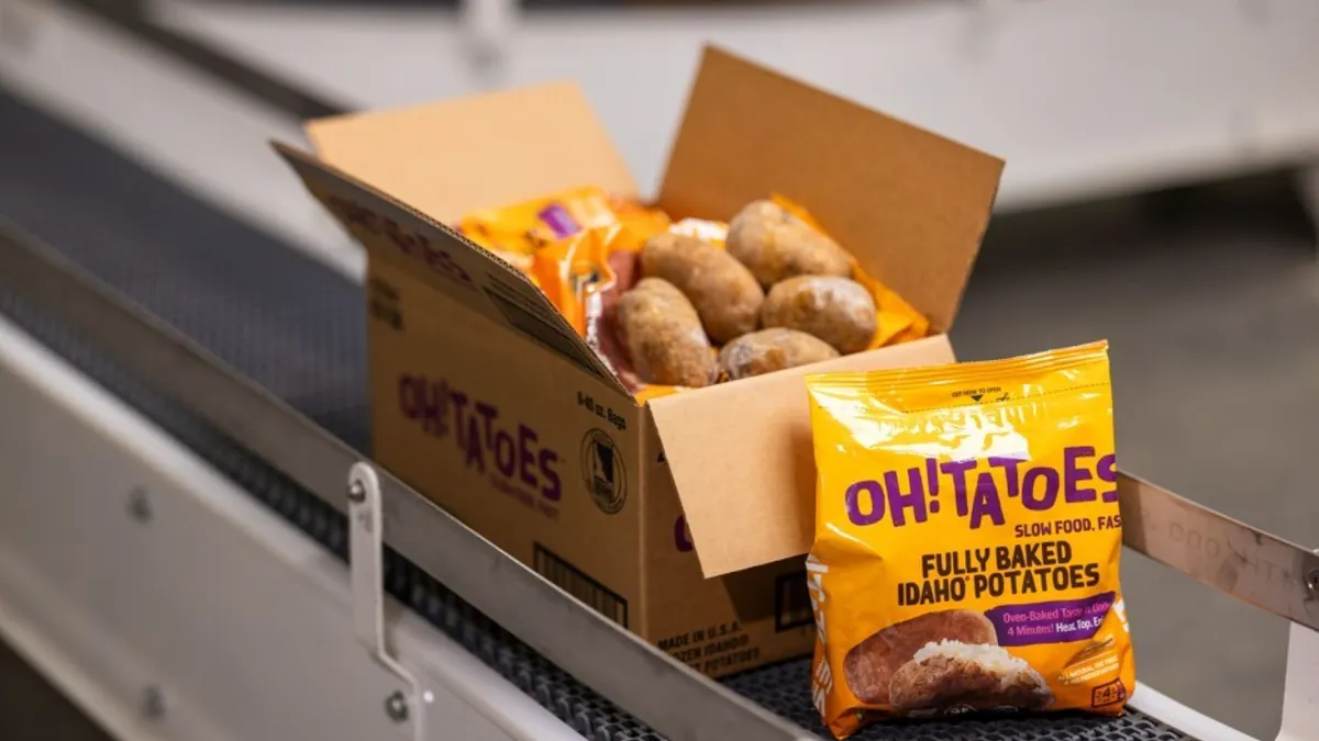 An unopened orange OH!Tatoes bag next to a box with an open bag on an assembly line.