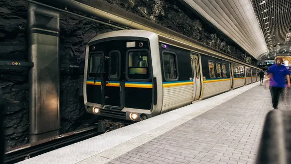 A silver and black train at an underground station with some people on the platform.
