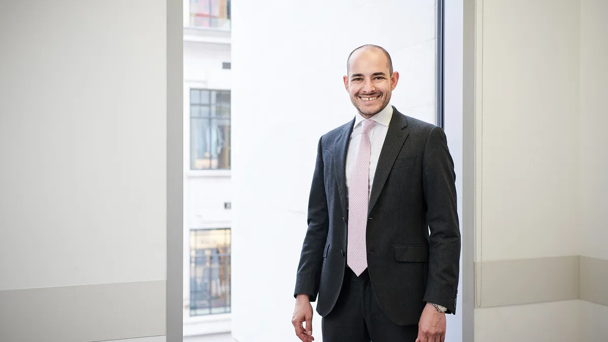 Patrick Saade wears a suit and stands in front of a window.