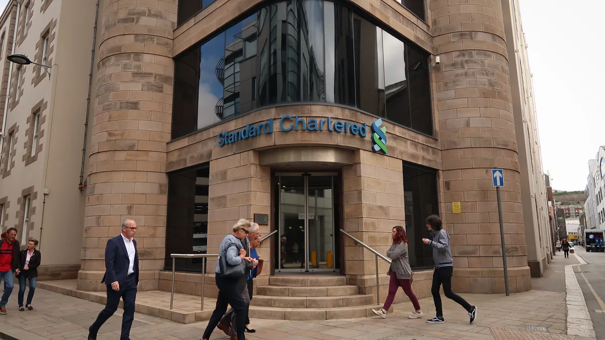 People pass the offices of Standard Chartered with the company's logo visible on the building.