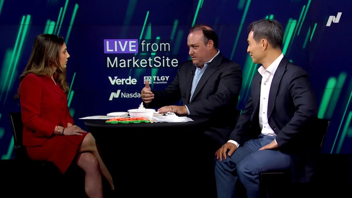 Three people sit around a table on a Nasdaq interview show, with a table containing Verde bioplastic products