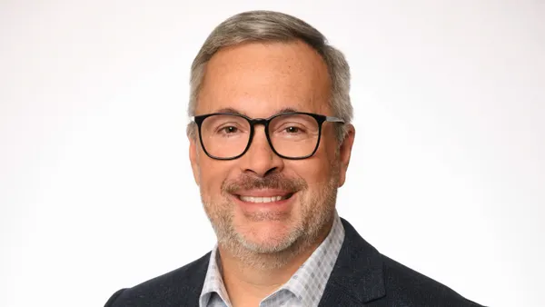 A photograph of a person wearing black glasses and a shirt and navy blazer.