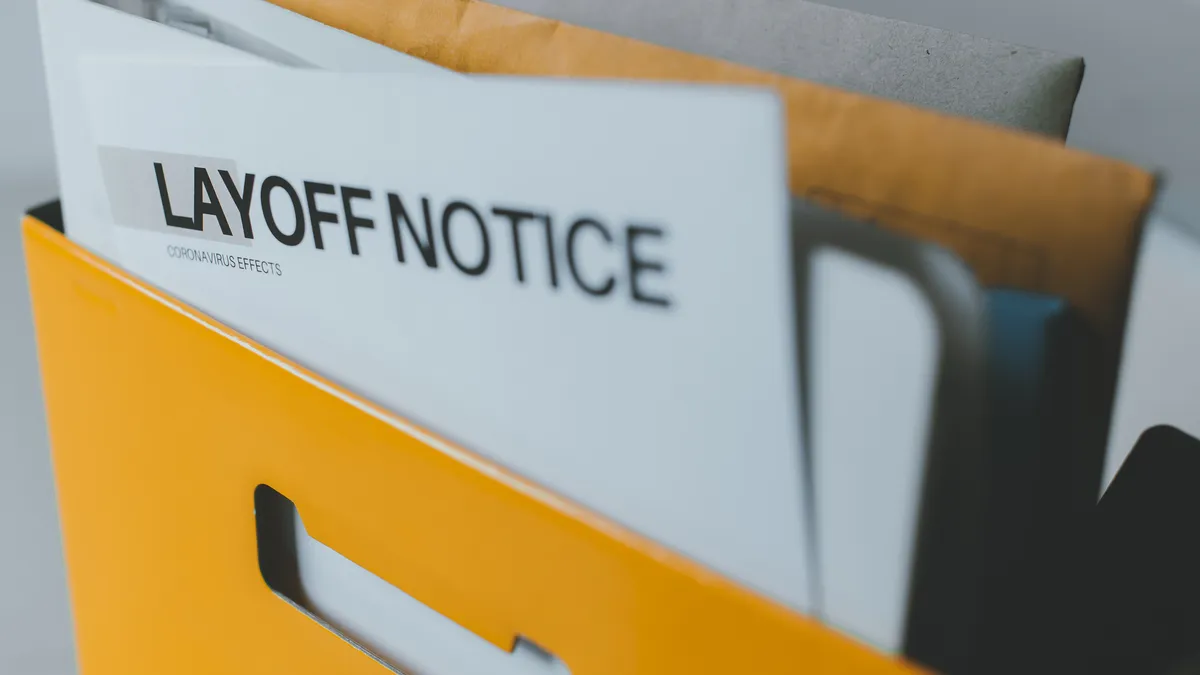 A paper reading "Layoff notice" in all caps sits in a yellow mailbox amongst other envelopes.