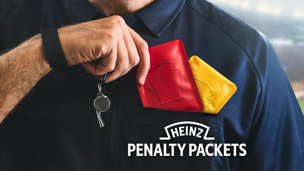 A ref, whose head is out-of-frame, reaches into his shirt pocket to pull out a red Heinz Penalty Packet.