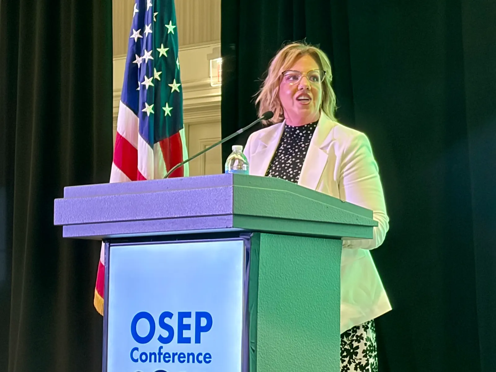 A person stands at a podium. A sign on the podium reads OSEP