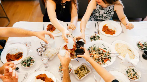 A family holds up glasses in cheer while eating at a Thanskgiving meal.