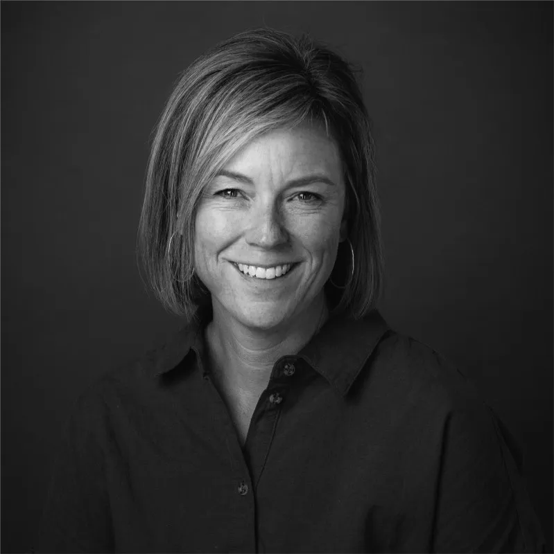 A person in a black shirt smiles at the camera in a black and white photo.