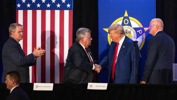 President Trump shaking hands on a stage in front of flag