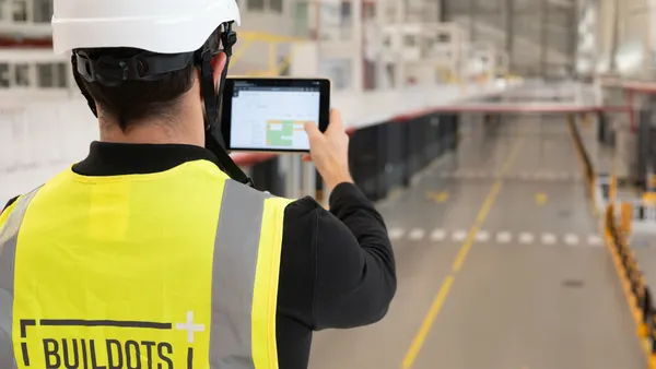 A shot of a person with yellow safety equipment on holding a tablet. "Buildots" is emblazoned on the back.
