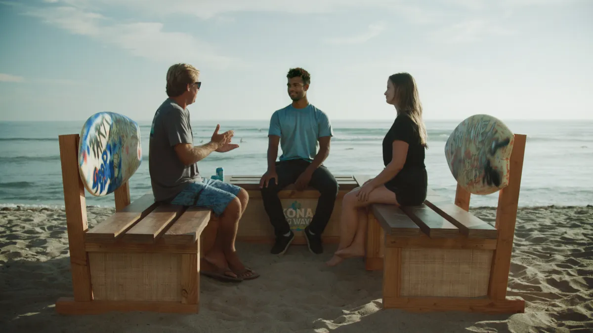 Three people sit on a bench on the beach.